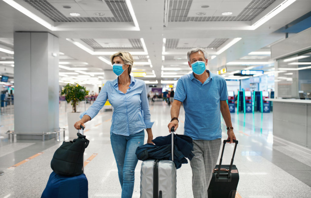 Grâce à leur certificat Covid, deux personnes masquées peuvent voyager et sont dans un aéroport, tirant des valises.
